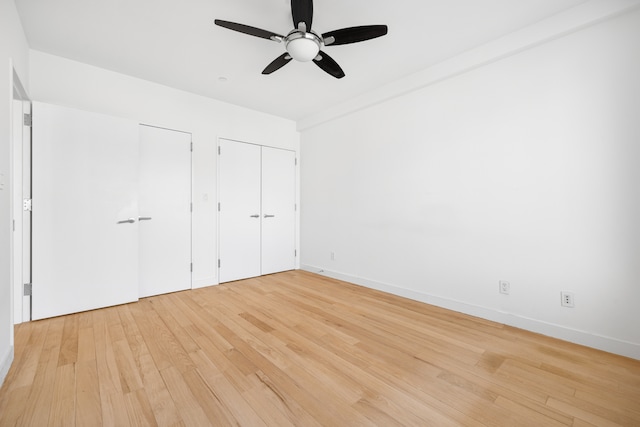 unfurnished bedroom featuring a ceiling fan, light wood-style flooring, baseboards, and multiple closets