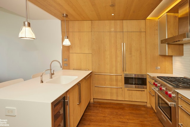 kitchen with a peninsula, a sink, high end stove, wall oven, and wall chimney exhaust hood