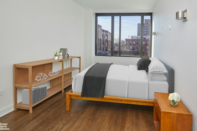 bedroom featuring wood finished floors, a view of city, and baseboards