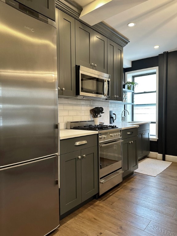 kitchen with light countertops, backsplash, appliances with stainless steel finishes, a sink, and wood finished floors