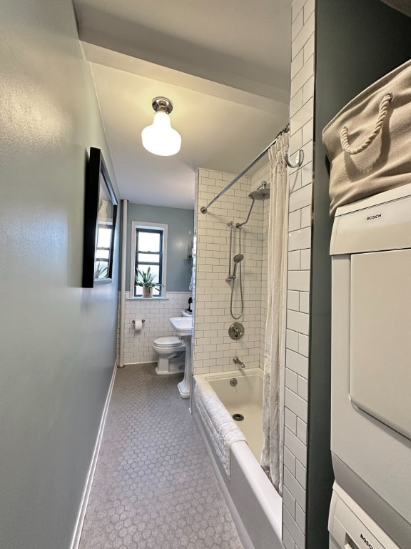 full bathroom featuring toilet, tile walls, stacked washer / drying machine, wainscoting, and shower / bath combo with shower curtain