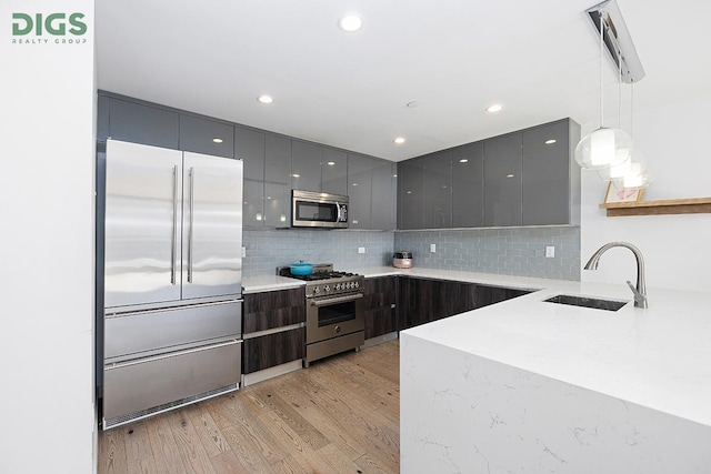 kitchen with premium appliances, modern cabinets, light wood-type flooring, pendant lighting, and a sink