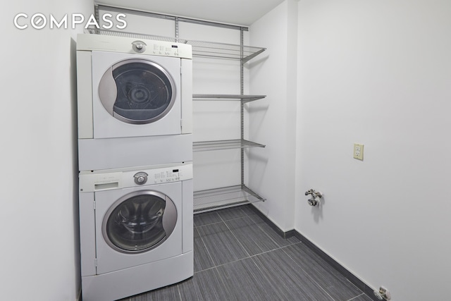 clothes washing area featuring dark tile patterned floors, laundry area, stacked washer and clothes dryer, and baseboards