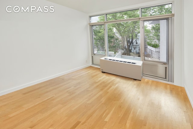 spare room with radiator heating unit, wood finished floors, and baseboards