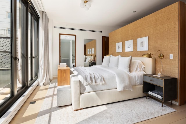 bedroom with multiple windows, wood finished floors, an accent wall, and wallpapered walls