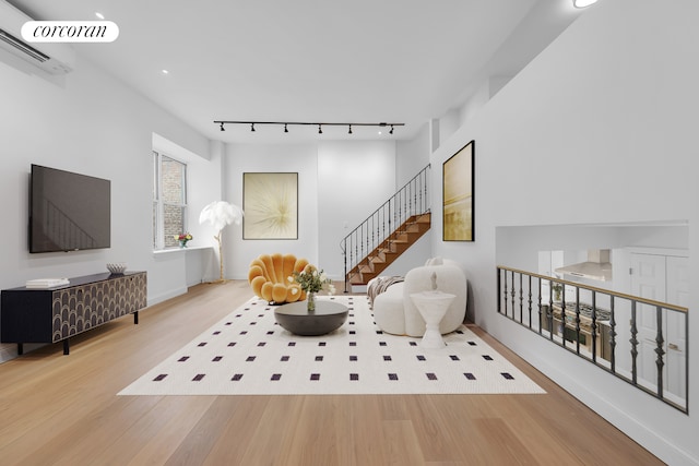 sitting room with track lighting, wood finished floors, a wall unit AC, baseboards, and stairs