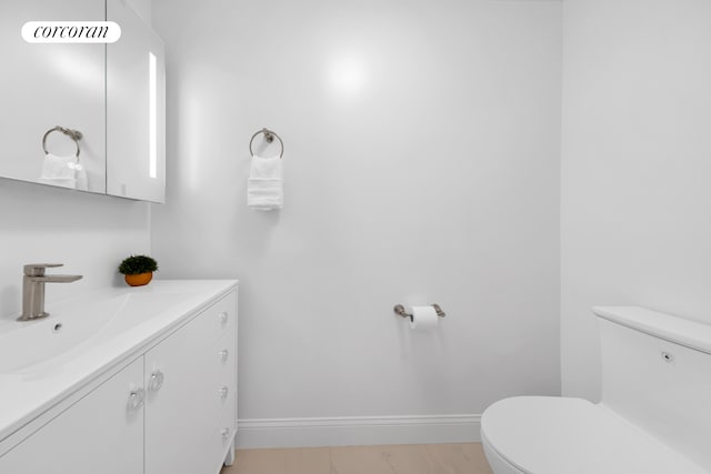 half bathroom with toilet, vanity, and baseboards
