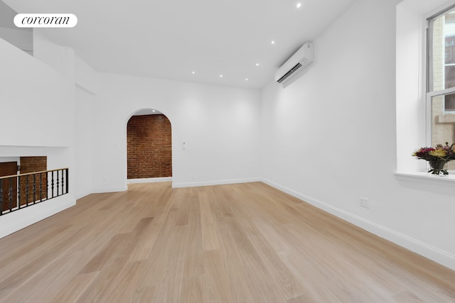 spare room with a wall unit AC, light wood finished floors, arched walkways, recessed lighting, and baseboards