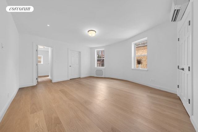 unfurnished bedroom with an AC wall unit, light wood-type flooring, and baseboards