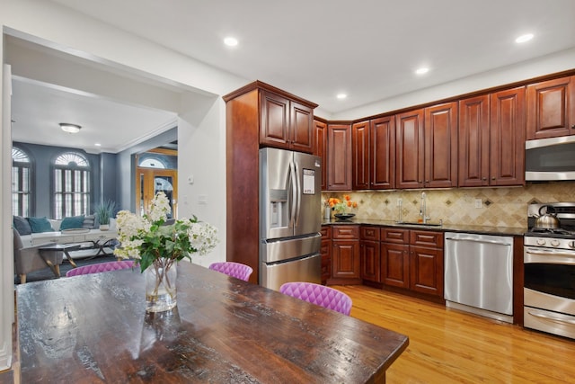 kitchen with appliances with stainless steel finishes, a sink, dark countertops, light wood-type flooring, and decorative backsplash