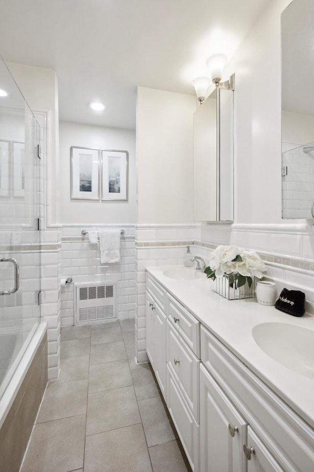 full bath with tile walls, tiled shower, radiator, double vanity, and recessed lighting
