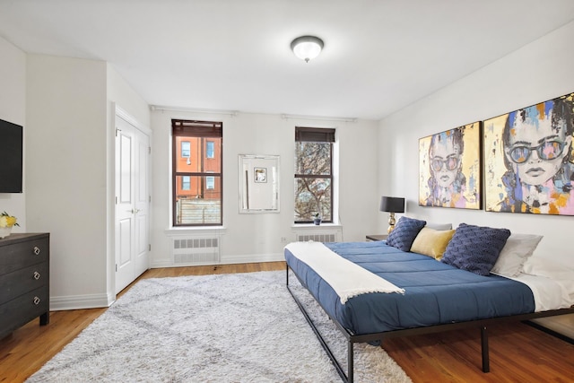 bedroom with radiator heating unit, wood finished floors, and baseboards