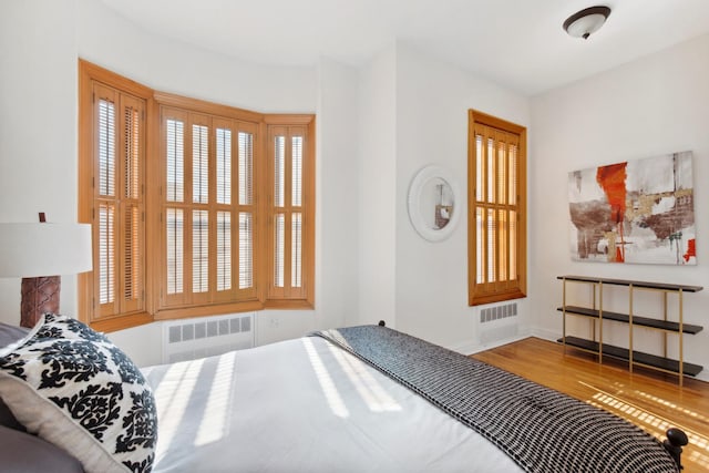 bedroom with radiator heating unit, wood finished floors, and baseboards
