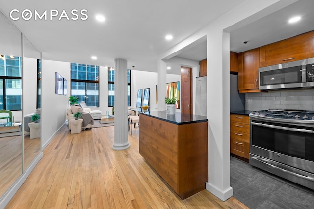 kitchen with stainless steel appliances, decorative backsplash, brown cabinetry, light wood-style floors, and open floor plan