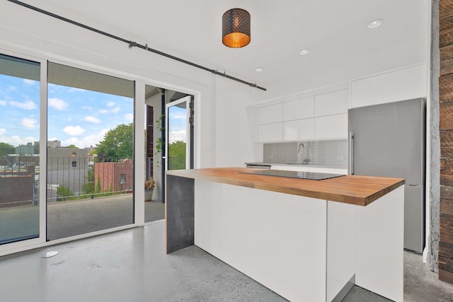 kitchen with freestanding refrigerator, decorative backsplash, butcher block countertops, a center island, and white cabinetry