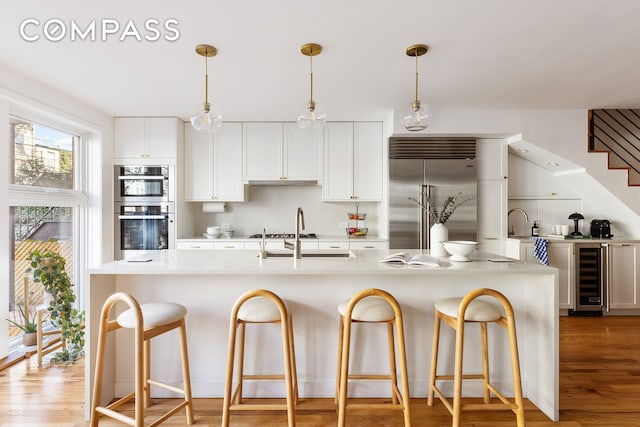 kitchen with beverage cooler, light wood-style flooring, light countertops, appliances with stainless steel finishes, and white cabinetry