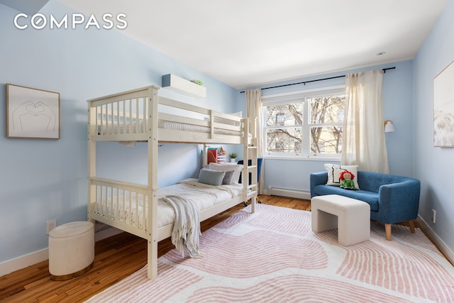 bedroom with a baseboard heating unit, wood finished floors, and baseboards