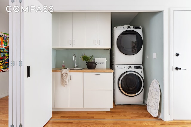 washroom with stacked washer / dryer, cabinet space, light wood-type flooring, and a sink