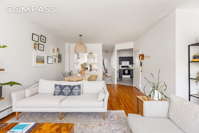 living room with a baseboard heating unit, wood finished floors, and stairs