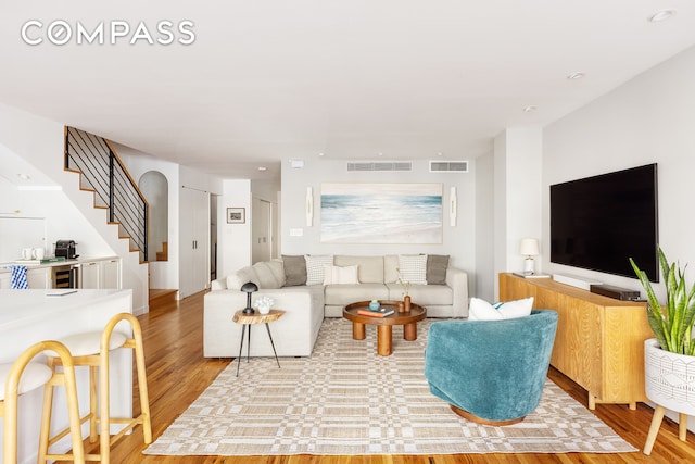 living room featuring visible vents, light wood-style flooring, and stairway