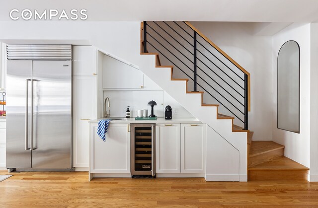 bar featuring stairway, light wood-style flooring, beverage cooler, and stainless steel built in fridge