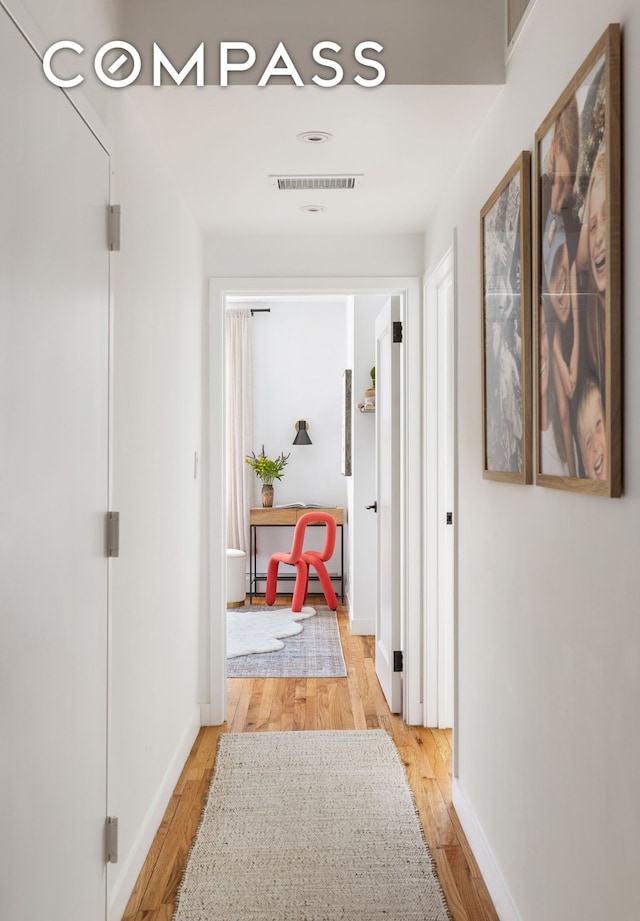 hallway featuring visible vents, baseboards, a baseboard heating unit, and light wood finished floors