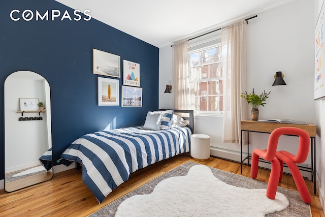 bedroom featuring wood finished floors, arched walkways, and baseboards