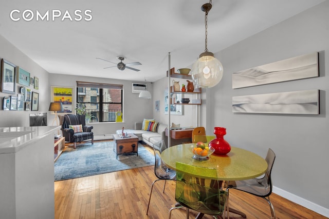 dining area featuring a wall mounted air conditioner, a ceiling fan, baseboards, and wood finished floors