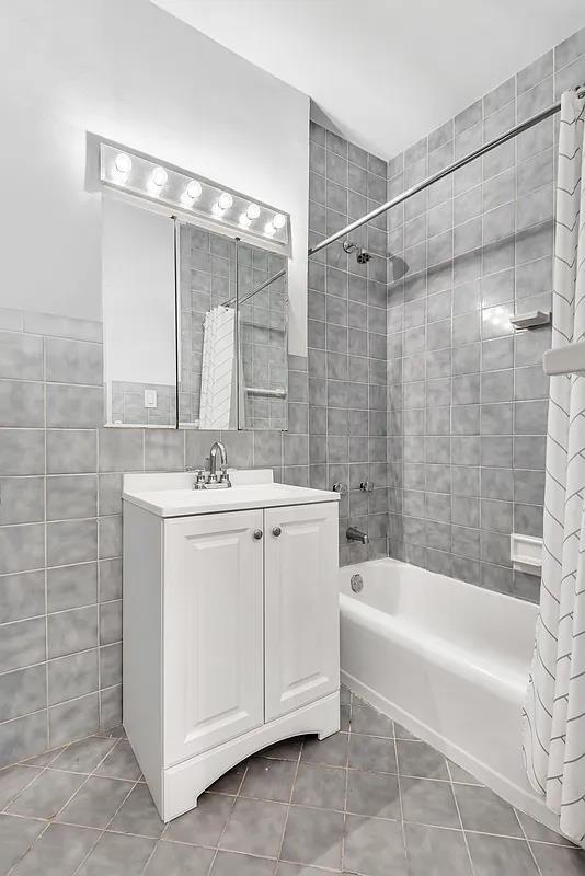 345 E 52nd St Unit 12A, New York City, NY 10022 - full bathroom featuring tile patterned floors, shower / bath combo with shower curtain, vanity, and tile walls
