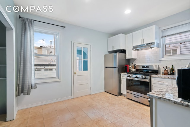 kitchen with light stone counters, backsplash, appliances with stainless steel finishes, white cabinetry, and under cabinet range hood