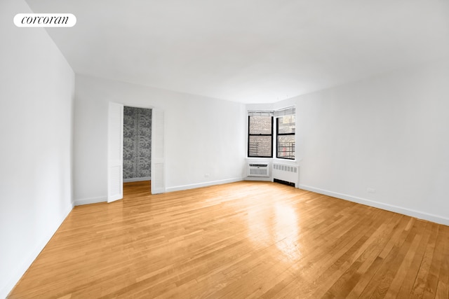 spare room featuring radiator heating unit, visible vents, light wood-style flooring, and baseboards