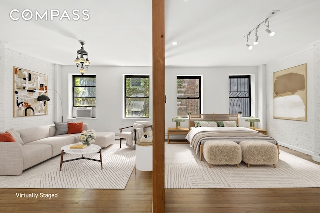 bedroom featuring cooling unit, wood finished floors, rail lighting, and baseboards