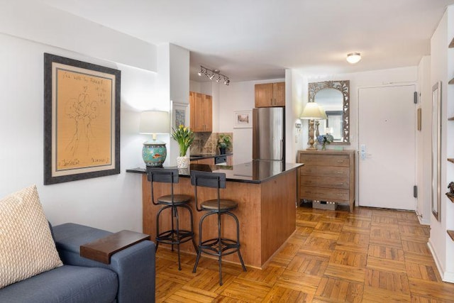 kitchen featuring brown cabinets, a breakfast bar, dark countertops, freestanding refrigerator, and a peninsula