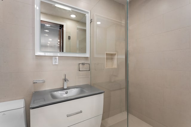 bathroom featuring vanity, tile walls, toilet, and tiled shower