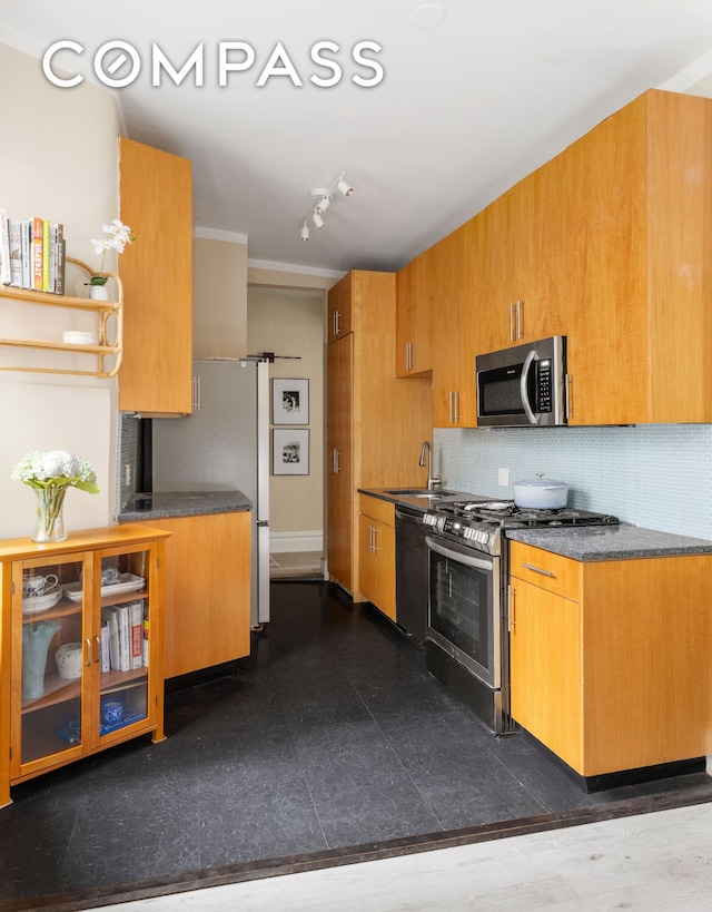 kitchen featuring dark countertops, backsplash, appliances with stainless steel finishes, and a sink