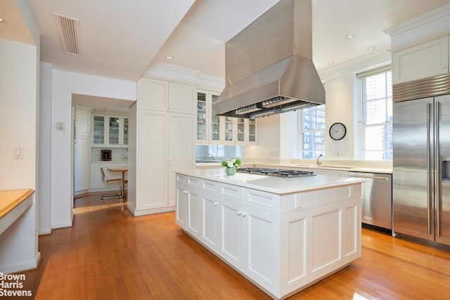 1 Beekman Pl Unit 7/8A, New York City, NY 10022 - kitchen featuring appliances with stainless steel finishes, island exhaust hood, light countertops, glass insert cabinets, and light wood-type flooring