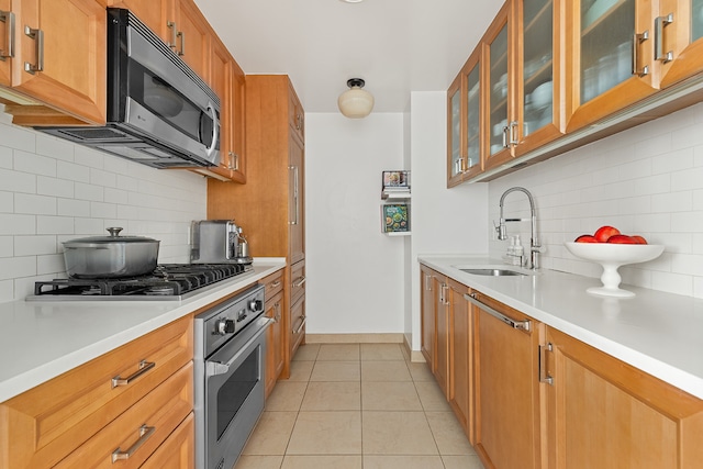 kitchen featuring light tile patterned floors, a sink, stainless steel appliances, light countertops, and brown cabinets