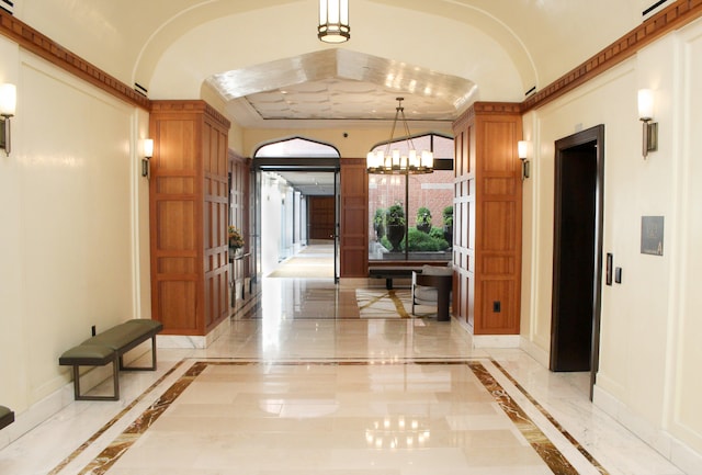 corridor with inlaid floor details, baseboards, a chandelier, and light marble finish flooring