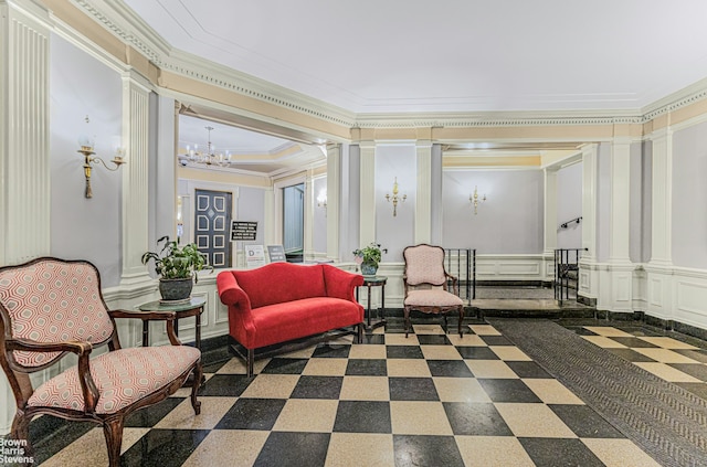 living area featuring a wainscoted wall, an inviting chandelier, crown molding, a decorative wall, and decorative columns