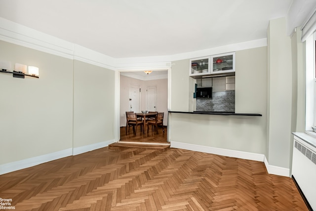 interior space with crown molding, radiator heating unit, glass insert cabinets, and baseboards