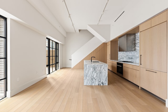 kitchen with light brown cabinetry, modern cabinets, wall chimney exhaust hood, and a sink