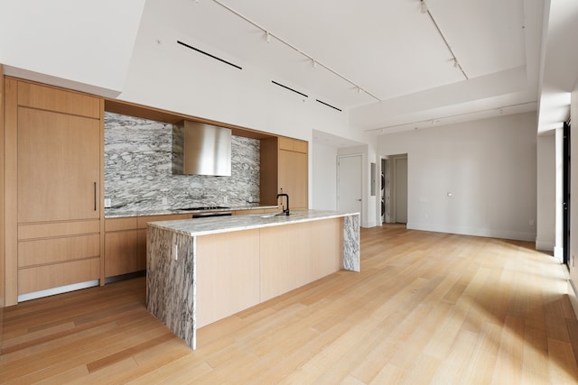 kitchen with modern cabinets, a sink, wall chimney range hood, light wood finished floors, and decorative backsplash