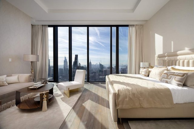 bedroom with a tray ceiling, a city view, and hardwood / wood-style flooring