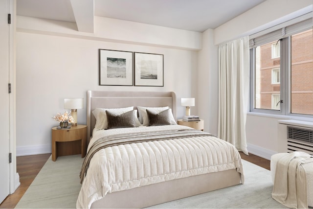 bedroom with baseboards, wood finished floors, and a wall mounted AC