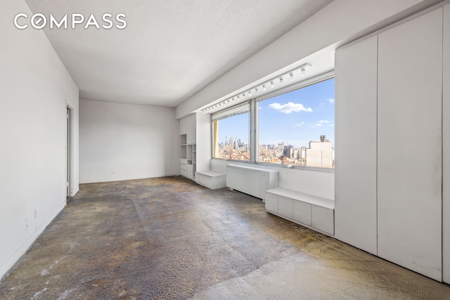 unfurnished bedroom with concrete flooring, a textured ceiling, a city view, and radiator heating unit