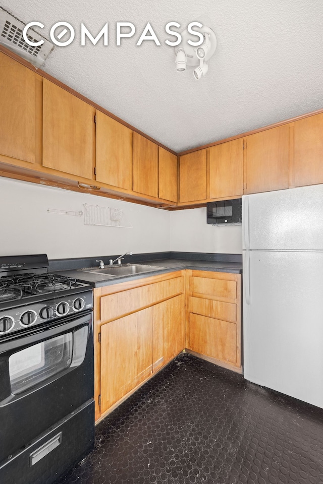 kitchen featuring a sink, dark countertops, a textured ceiling, freestanding refrigerator, and gas stove