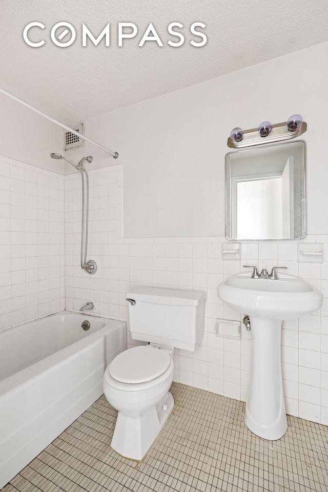 bathroom with tile walls, shower / washtub combination, toilet, tile patterned floors, and a textured ceiling