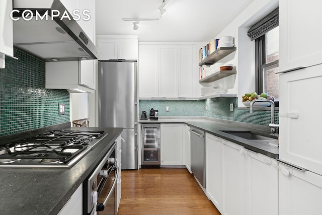 kitchen with a sink, wine cooler, under cabinet range hood, appliances with stainless steel finishes, and white cabinetry