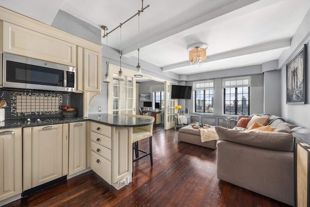 kitchen with a breakfast bar, a peninsula, cream cabinetry, stainless steel microwave, and open floor plan