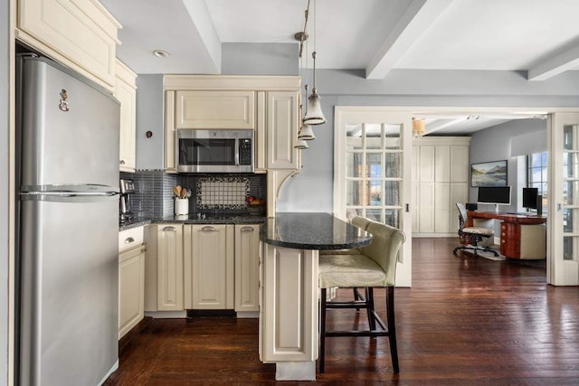 kitchen featuring decorative backsplash, beam ceiling, cream cabinets, and appliances with stainless steel finishes